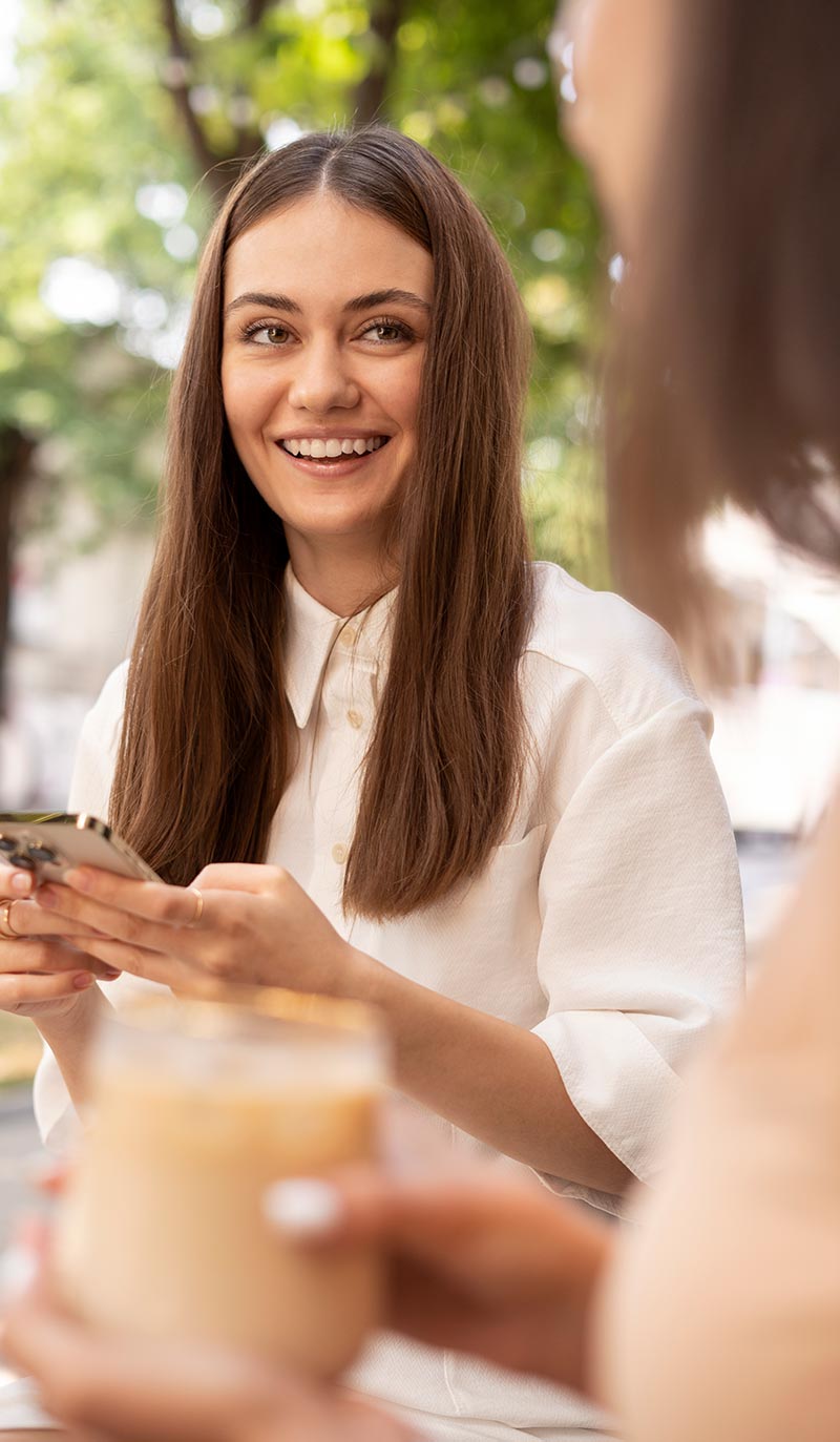Woman holding a phone and smiling outdoors