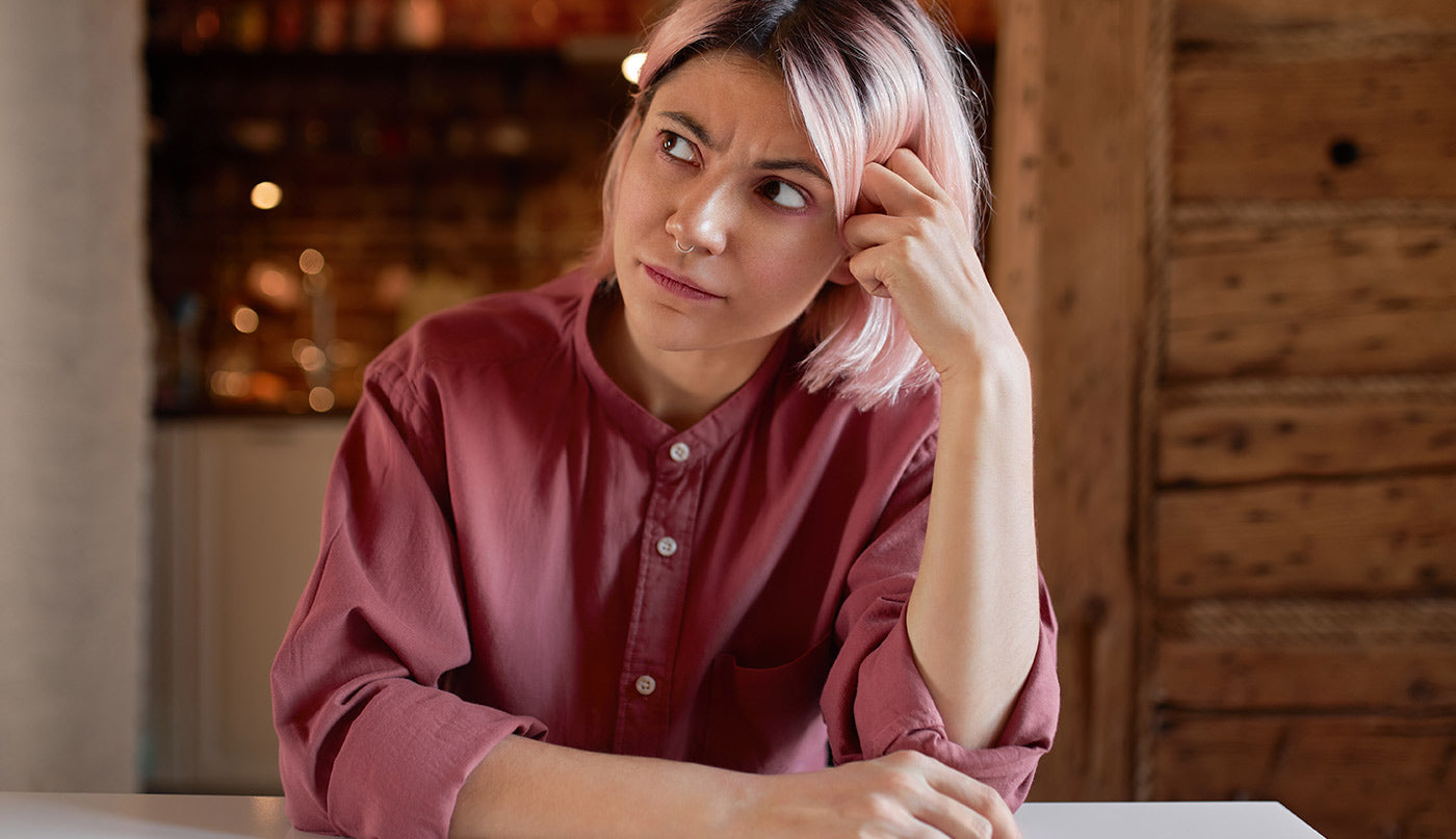 Woman in a maroon shirt sitting at a table with a blurred background thinking about quitting vaping.