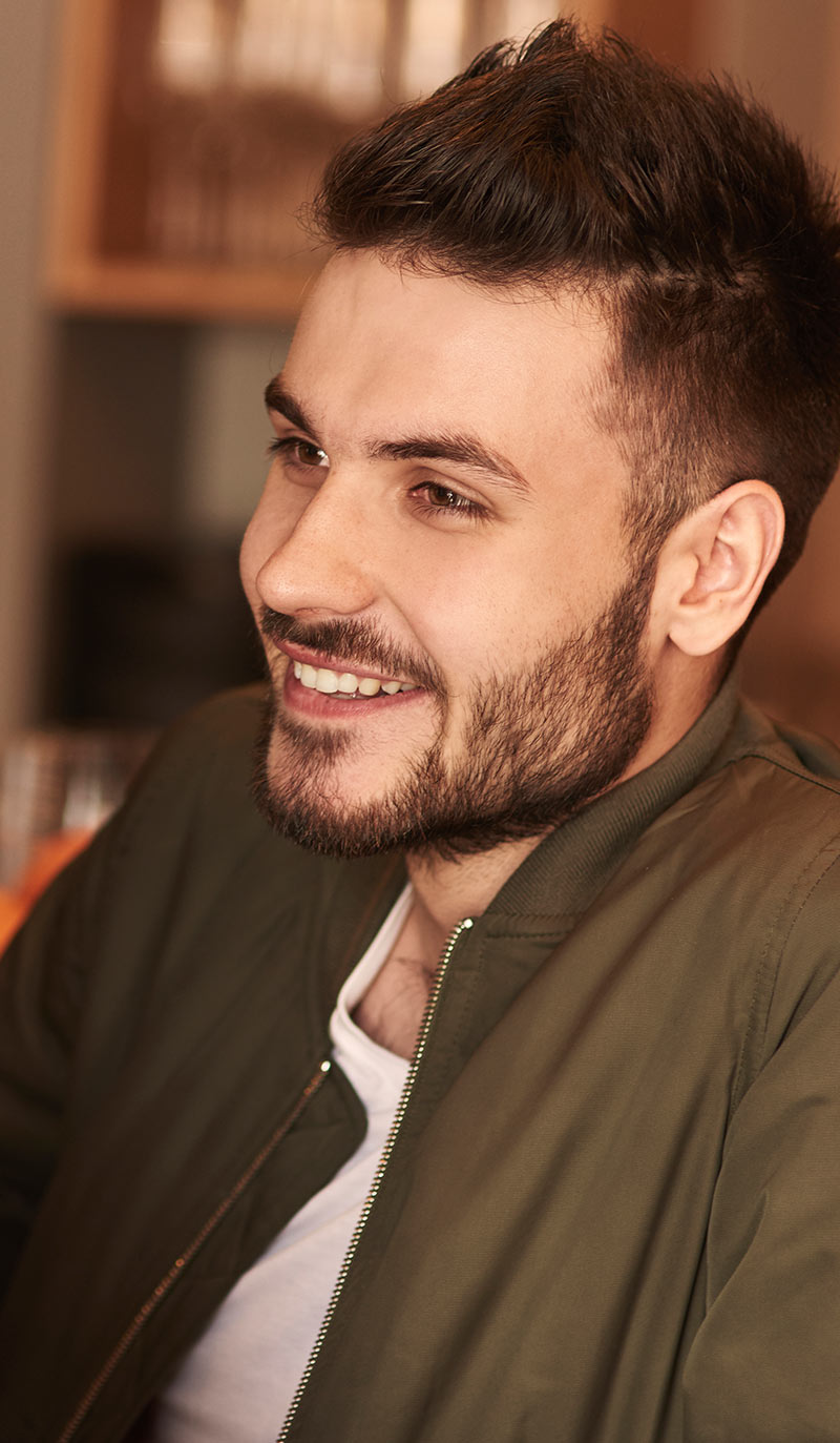 Man with a beard wearing a green jacket indoors explaining the difference between smoking and vaping