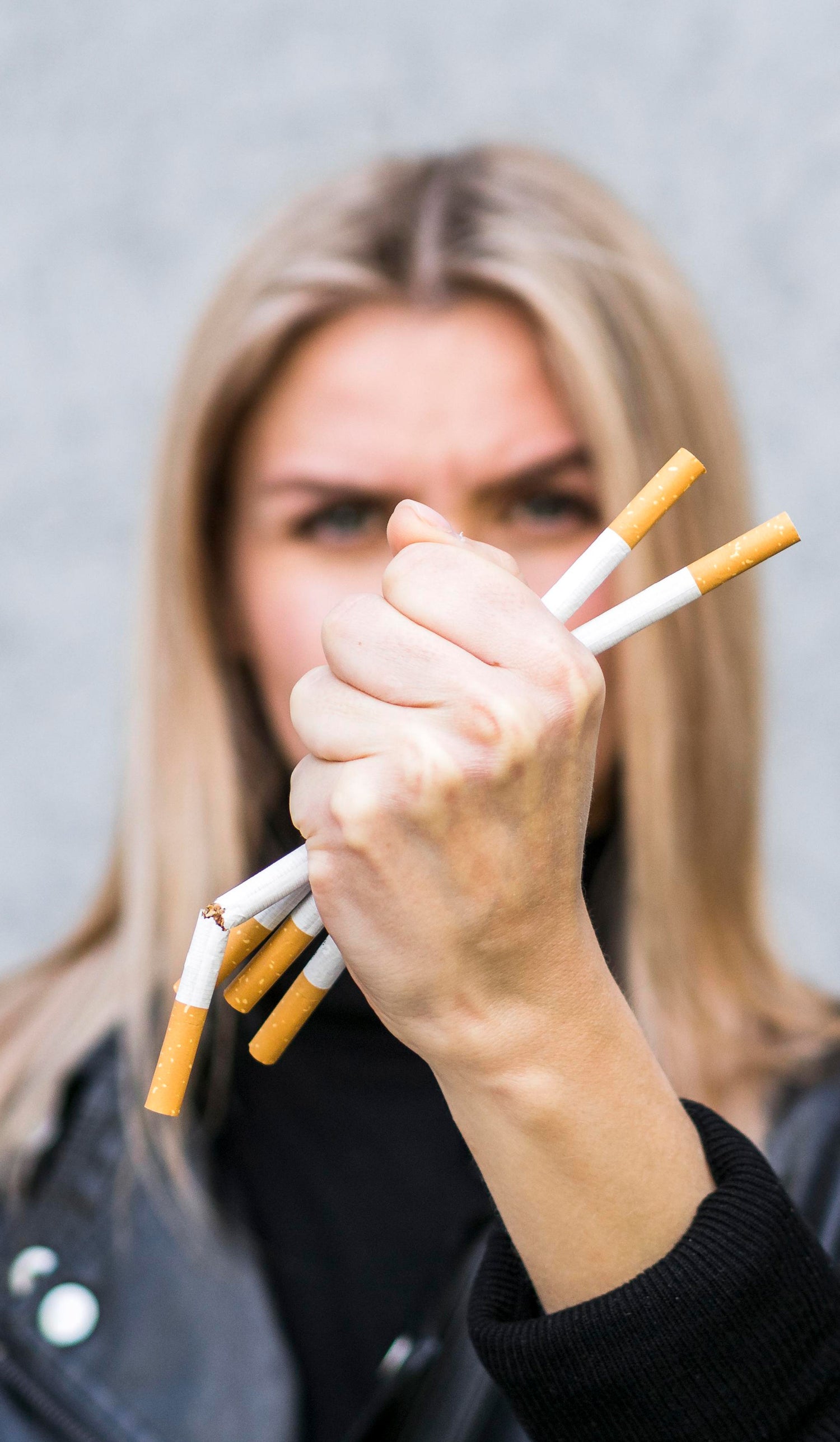Woman holding multiple cigarettes with a determined expression against a gray background
