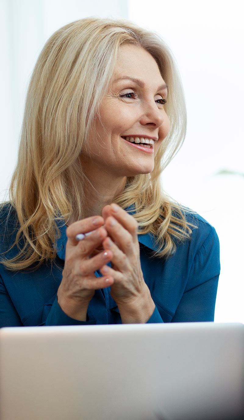 Quit smoking nurse with blonde hair and blue shirt sitting in front of a laptop, smiling.