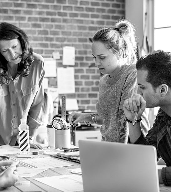 Three people working together at a table with a laptop in an office setting.