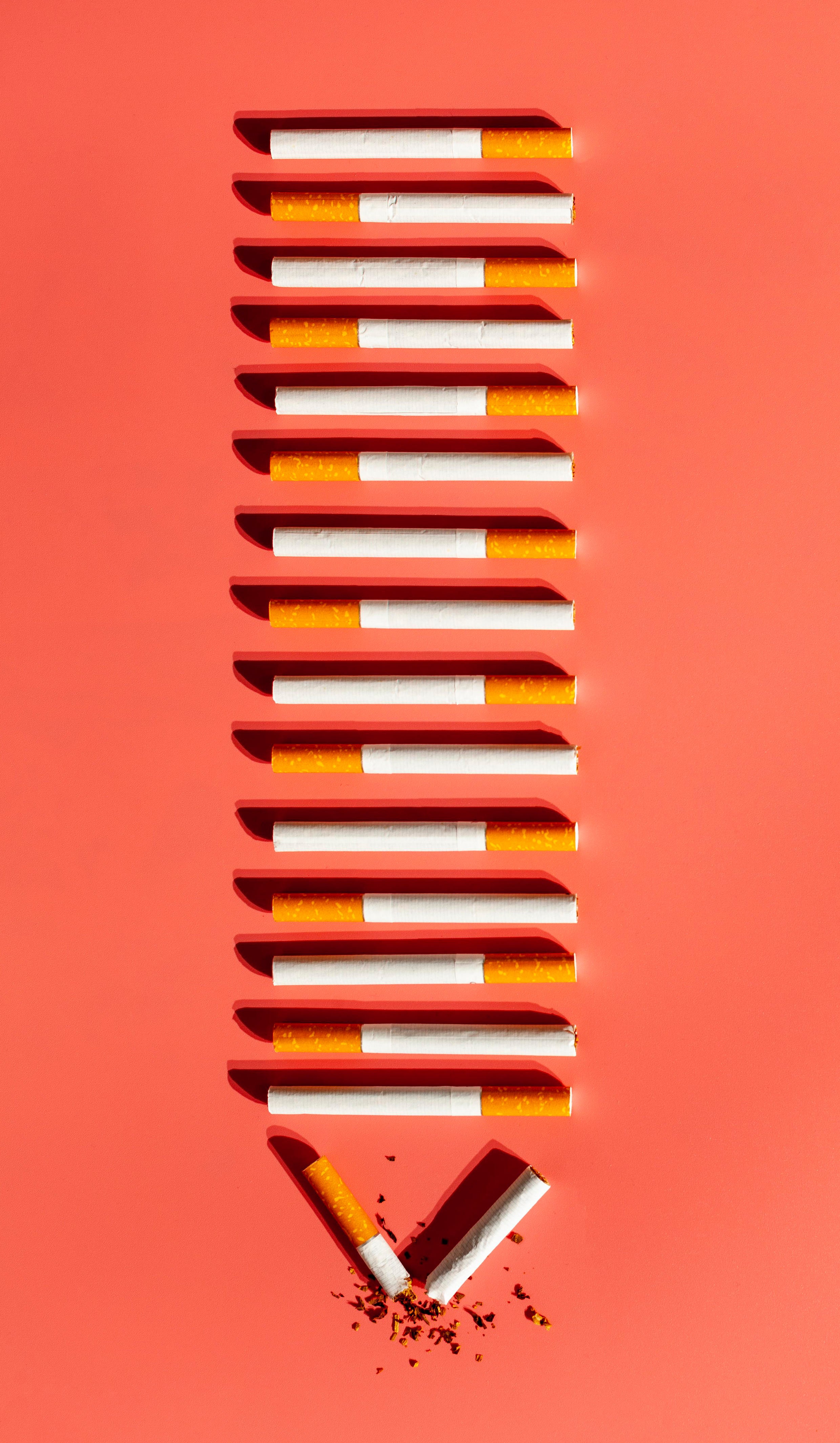 Cigarettes arranged vertically on a red background with one cigarette broken at the bottom.