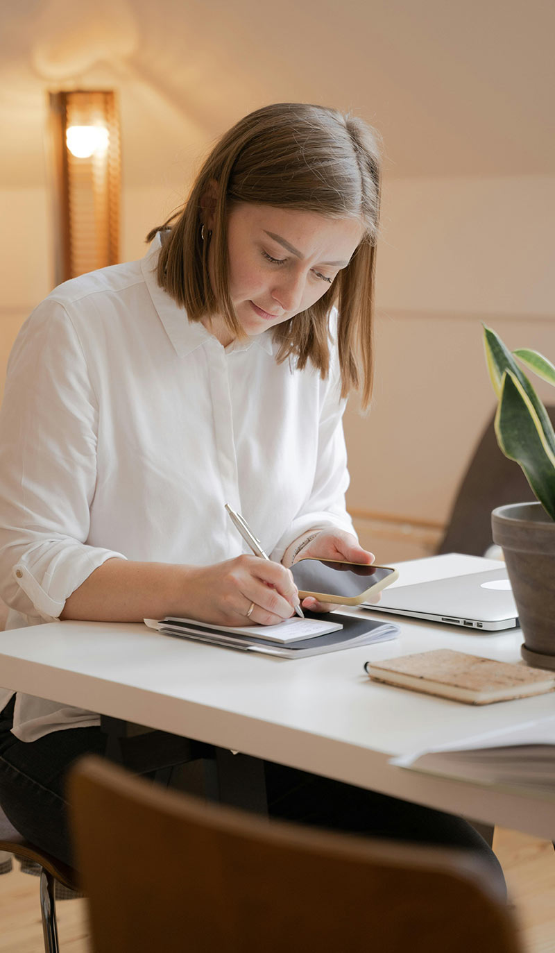 Woman sitting at a desk with a tablet and phone, writing down how many cigarettes she has a day.