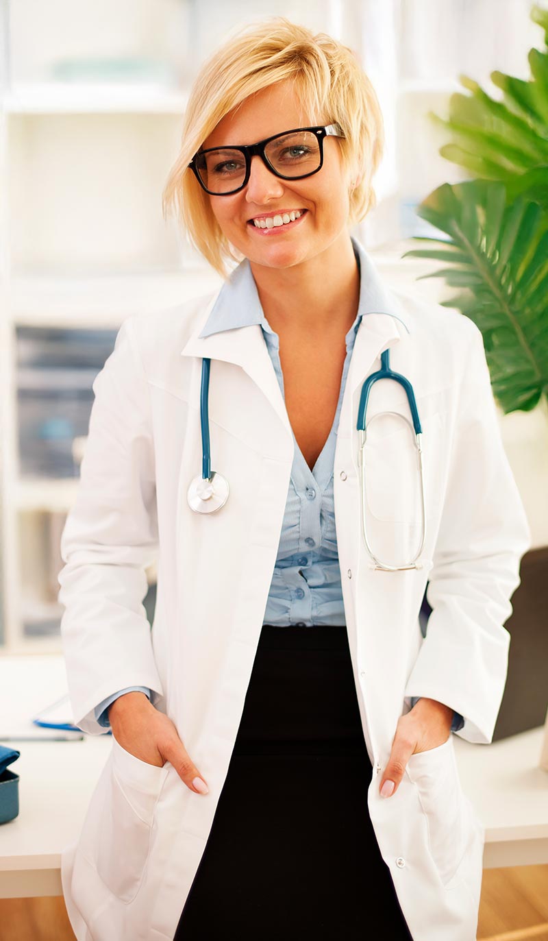 Doctor wearing a white coat with a stethoscope, standing in a medical office.
