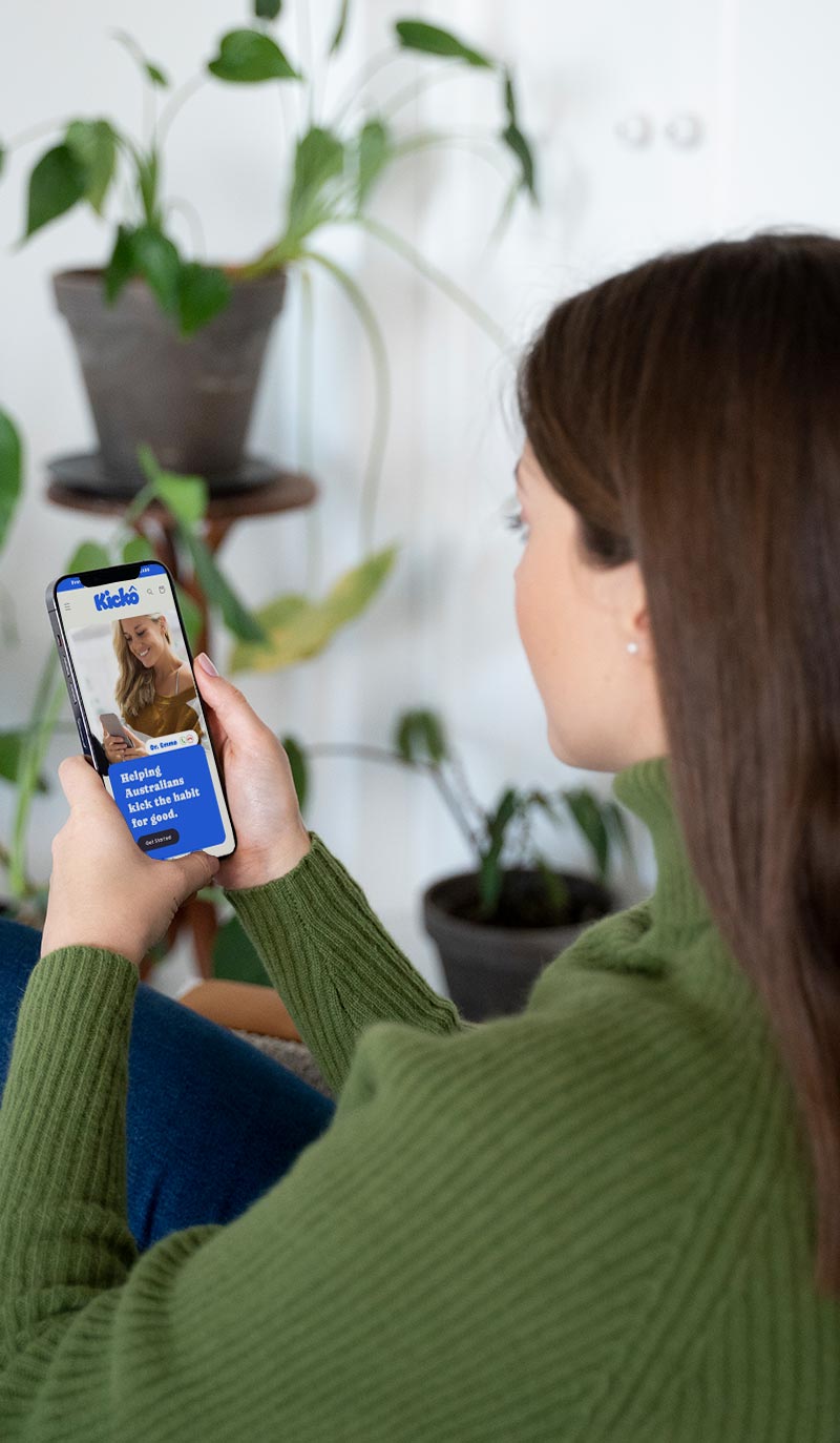 Person holding a smartphone with a home screen displaying an app, sitting in a room with plants.