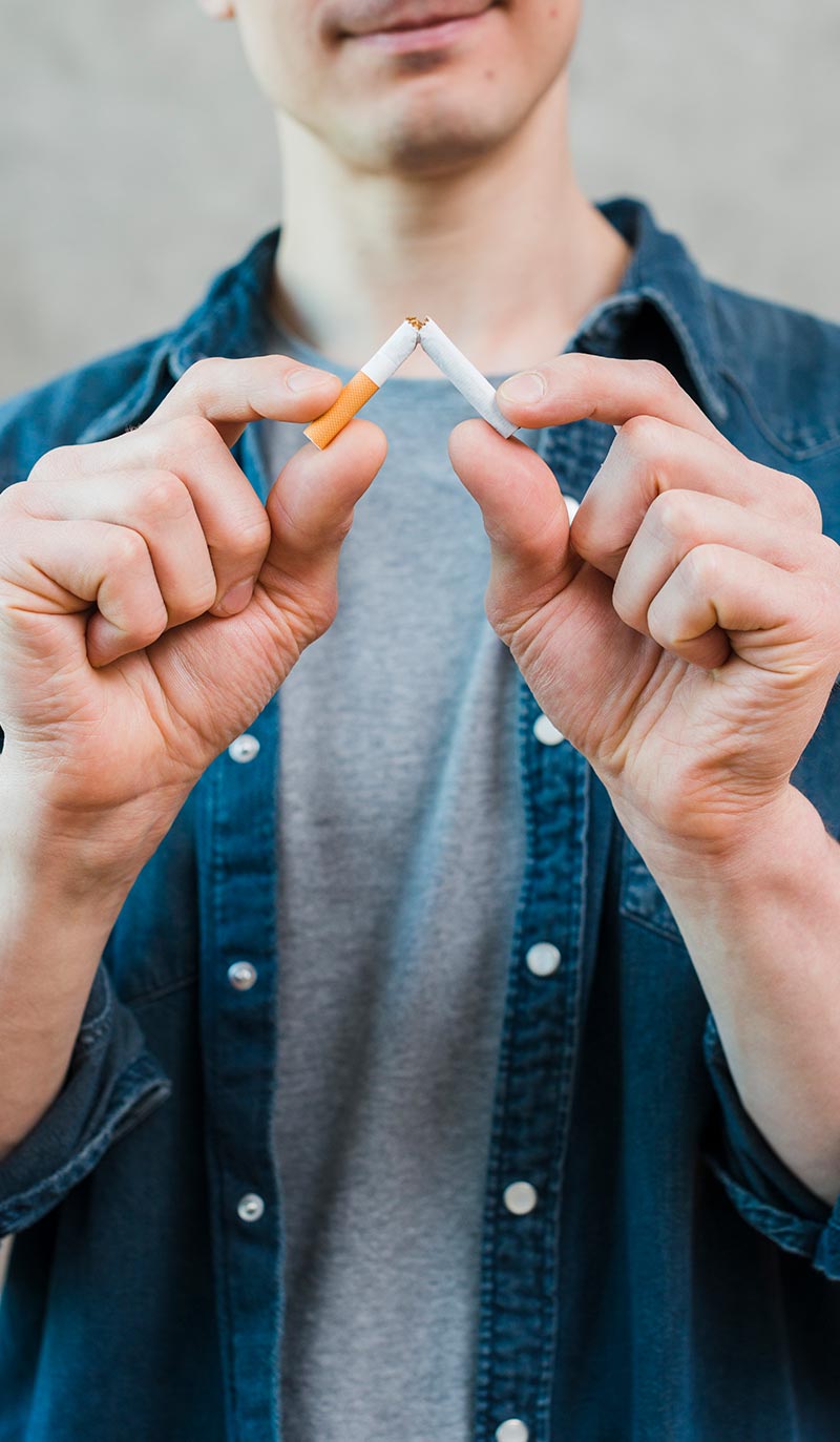 Person holding two cigarettes, one intact and one being lit, against a neutral background.