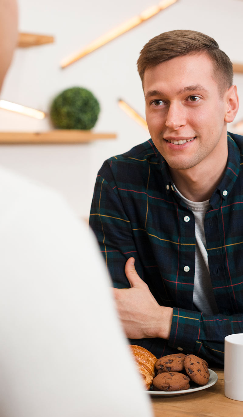 Man sitting at a table trying to quit smoking with cookies and a mug, smiling.