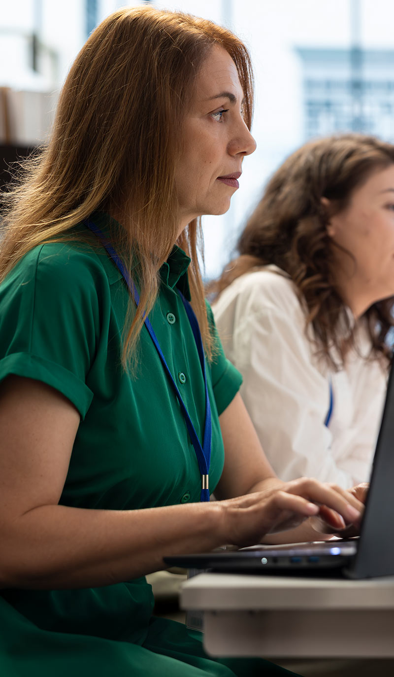 Doctor in green shirt using a laptop with another person in the background.